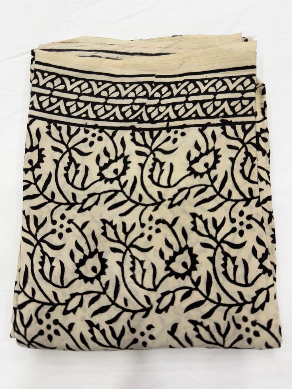 Premium quality unstitched cream Santoon silk bottom fabric adorned with delicate black hand block printed branch and leaf patterns, neatly rolled for the mustard suit set.
