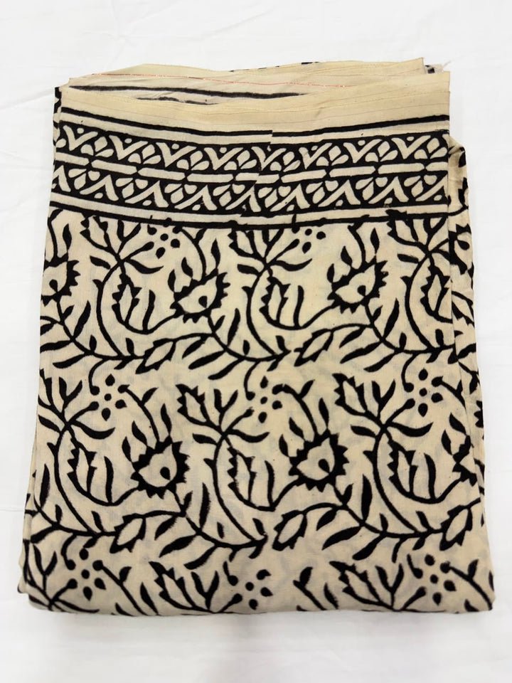Premium quality unstitched cream Santoon silk bottom fabric adorned with delicate black hand block printed branch and leaf patterns, neatly rolled for the mustard suit set.