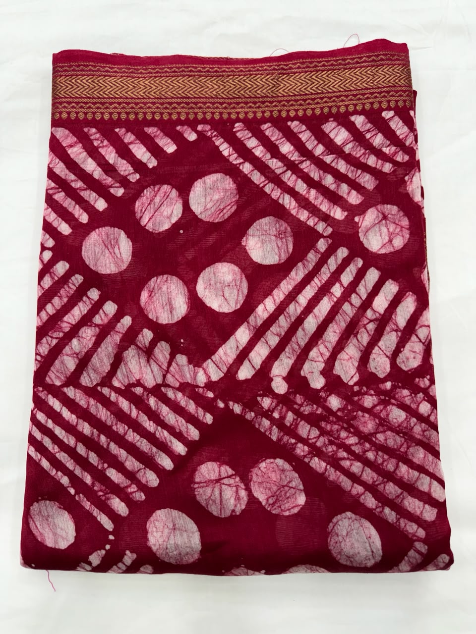 Close-up of the unstitched red Maheshwari silk kurta fabric, featuring traditional wax-resist batik hand block printed geometric patterns in crisp white.