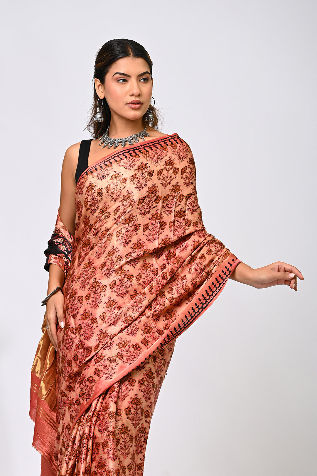 An authentic plant-based Vanaspati dyed Modal Silk saree in natural brick red and black, showing the fluid drape and intricate hand block prints against a plain white background.