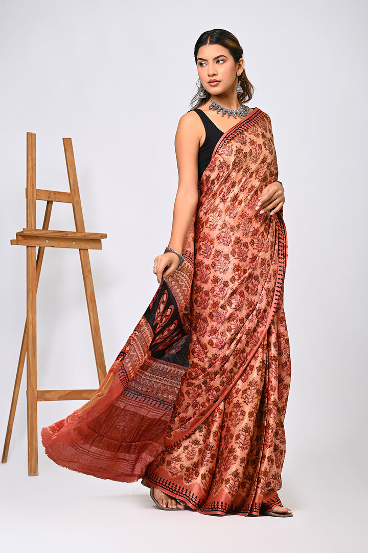 An authentic plant-based Vanaspati dyed Modal Silk saree in natural brick red and black, showing the fluid drape and intricate hand block prints against a plain white background.