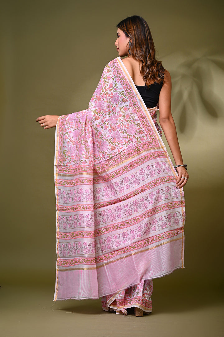 Back view of a woman modeling a baby pink Sanganeri print Chanderi Silk saree, showcasing the flowing drape of its intricate floral jaal lattice pattern and a detailed border next to a wooden easel.