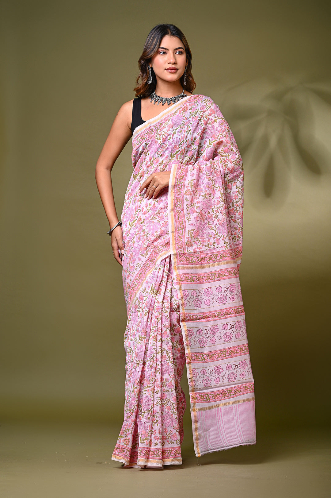 A woman modeling a baby pink Sanganeri print Chanderi Silk saree featuring an all-over intricate floral jaal lattice pattern, structured borders, and a matching patterned pallu against a soft olive green backdrop.