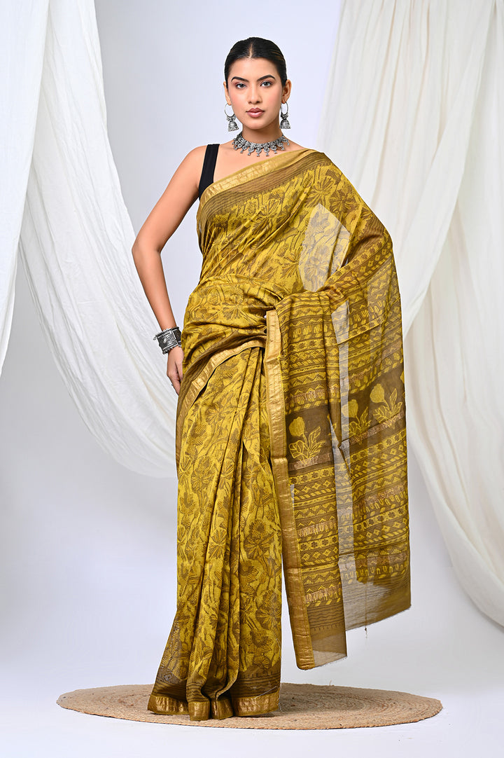 A woman modeling a natural mustard yellow Maheshwari silk saree featuring an intricate geometric block print design, a traditional patterned pallu, and a classic border.