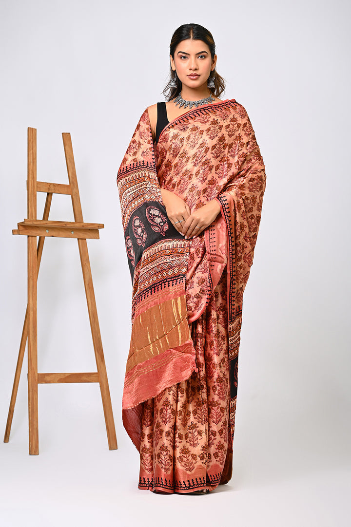 A woman modeling a natural red Vanaspati print Modal Silk saree featuring a detailed black and cream floral vine design, traditional Lagdi Patta borders, and a large paisley motif on the pallu.